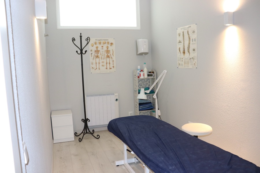 Sala de tratamiento luminosa con camilla y láminas anatómicas